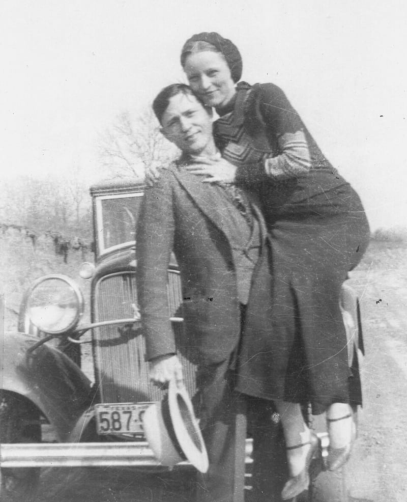 Bonnie Parker leaning on Clyde Barrow’s shoulder as they pose in front of a car, about 1933